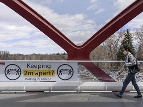 A masked pedestrian walks by a sign encouraging people to stay two meters apart on Peace Bridge on Wednesday, April 28, 2021.
