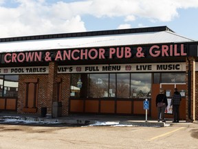 Two people look into the Crown and Anchor Pub at Grill at 15277 Castle Downs Rd NW in Edmonton, on Monday, April 12, 2021. The owners have decided to shut the pub down after one day of staying open despite public health orders after they said staff had received threats.