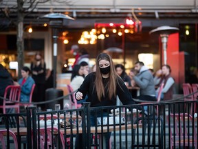 A masked server clears a table on a patio at a restaurant in Vancouver on April 2, 2021.