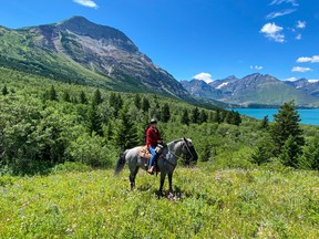 An image of a woman riding a grey horse in Waterton Lakes National Park, Alberta, Canada. Vimy Peak is in the background.