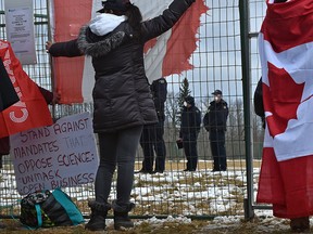 A woman holds up a tattered Canadian flag as police stand by while a crowd of about 400 gathered outside GraceLife Church on the first Sunday after the closure west of Edmonton, April 11, 2021.