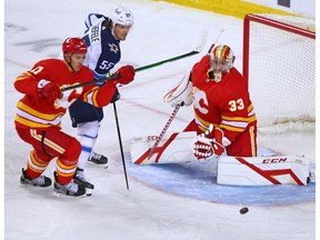 Calgary Flames goaltender David Rittich keeps his eyes on a puck with the Winnipeg Jets’ Mark Scheifele and the Flames’ Mikael Backlund at the Saddledome in Calgary on Saturday, March 27, 2021.