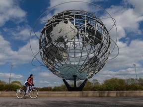 A boy rides his bike past the Unisphere, a stainless steel representation of the Earth, in Flushing Meadows Corona Park on Earth Day, April 22, 2021 in New York City.