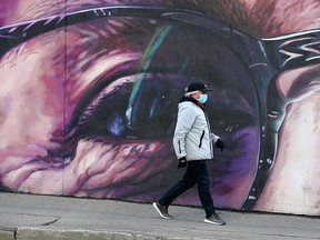 A masked pedestrian walks past a mural along MacLeod Trail S.W. in Calgary on  Monday, April 19, 2021.