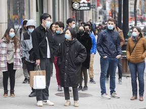 People wearing face masks await to cross a street in Montreal on March 27, 2021.