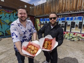 Ray Burton, left, general manager, and Alex Durant, Chef/hot dog enthusiast, with Lost Dogs hot dogs pose for a photo in a back alley in Beltline on Thursday, April 29, 2021.  Burton is holding The Chinook Dog with Malt Vinegar Potato Chips and Durant is holding The Prince's Island Dog with Waffle Fries. Azin Ghaffari/Postmedia