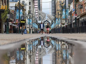 Stephen Avenue is reflected in a small puddle as people walk by on Thursday, May 13, 2021.