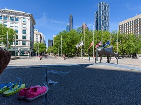 Flags outside Calgary City Hall are lowered to half-mast on Monday, May 31, 2021 after the discovery of the remains of 215 children at a former residential school in Kamloops. Some kids' shoes placed during a vigil are seen in the foreground.