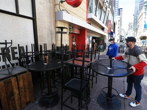 Kevin Warner, right with The Unicorn pub stacks patio tables and chairs on Monday, May 10, 2021. As of midnight Sunday new pandemic restrictions limit Calgary restaurants to takeout and delivery only.