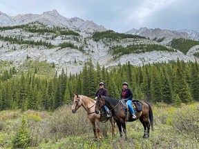 An image of a man and a woman on horseback with the Sundance Mountain Range in the background in Banff, Alberta, Canada.