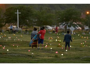 A family walks through a field where flags and solar lights now mark the site where human remains were discovered in unmarked graves at the former Marieval Indian Residential School site on Cowessess First Nation, Saskatchewan on June 26, 2021. More than 750 unmarked graves have been found near a former Catholic boarding school for Indigenous children in Western Canada, a tribal leader said, the second such shock discovery in less than a month.