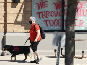 A woman and her service dog walk past a grocery store window in Osborne Village in Winnipeg on Thursday, June 17, 2021.