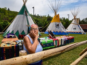 Annie Wesley poses for a photo with an exhibition of the traditional outfits she has made for her children behind her outside her teepee at the Calgary Stampede’s Elbow River Camp on Sunday, July 11, 2021.