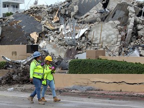 Rescue workers walk past debris after the managed demolition of the remaining part of Champlain Towers South complex as search-and-rescue efforts continue in Surfside, Florida, U.S. July 6, 2021.