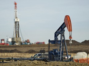 A pumpjack with a drilling rig in the background at a work site in Alberta.