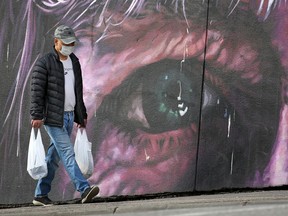 A masked shopper walks by a mural in downtown Calgary on Monday, April 20, 2020.