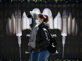 People wearing protection masks walk by a banner showing syringes as vampire fangs during the vaccination marathon organised at the "Bran Castle" in Bran village on May 8, 2021.