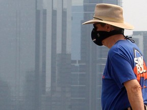 A man wearing a mask is seen walking along McHugh Bluff with office towers in the background as wildfire smoke continues to effect air quality in Calgary on Wednesday, Aug. 4, 2021.