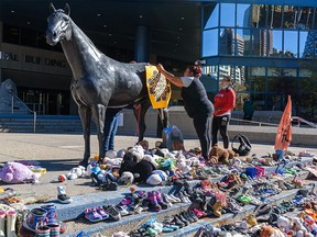 On Wednesday, September 29, 2021, Yvonne Henderson, left, and Auggie Hunter with Bear Clan Patrol Calgary attach a poster to one of the statues outside City Hall in preparation for September 30’s vigil on National Day for Truth and Reconciliation.