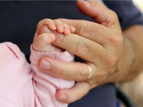 Close up on the hand of a newborn baby girl holding the finger of her Grandpa lovingly.