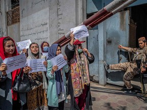 A Taliban fighter watches as Afghan women hold placards during a demonstration demanding better rights for women in front of the former Ministry of Women Affairs in Kabul on September 19, 2021.