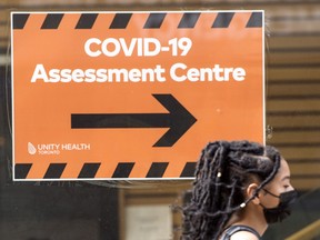 A pedestrian wearing a mask passes a COVID-19 assessment centre sign outside Toronto's St. Michael's Hospital on Friday, Aug. 27, 2021.