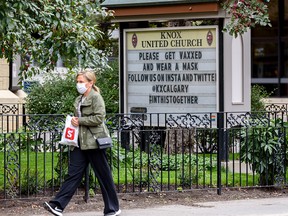 A masked pedestrian walks by a sign outside Knox United Church in downtown Calgary encouraging people to get vaccinated on Friday, Sept. 17, 2021.