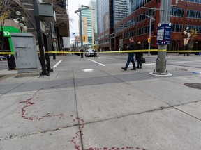 People walk around the blood trail left at the scene of a stabbing that took place earlier in the morning in downtown Calgary on Friday, October 15, 2021.