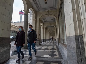 Masked pedestrians walk under the Hudson Bay’s store archway in downtown Calgary on Monday, October 25, 2021.