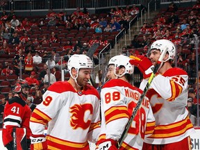 Flames forward Andrew Mangiapane (centre) celebrates his second goal of the game at 12:56 of the first period against the Devils with teammates Dillon Dube and Noah Hanifin at the Prudential Center on Tuesday night in Newark, N.J.