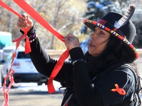 Deborah Green hangs a red ribbon in a tree in the Field of Crosses. Earlier this week ribbons honouring the lives of missing and murdered Indigenous women and girls had been cut off trees near the Field of Crosses and found in the garbage. Saturday a ceremony was held to rehang hundreds of red ribbons.