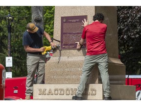 Workers remove a plaque on the monument that held the statue of Sir John A. Macdonald in Kingston, Ontario on Friday June 18, 2021. The statue will be removed from a park in his hometown of Kingston while his name will be taken off a local school.  Kingston's city council voted this week to take the statue from City Park, place it temporarily in storage, and eventually put it up in Kingston Cataraqui Cemetery where Canada's first prime minister is buried.