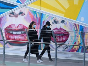Masked pedestrians walk by Corridor of Connection Mural at the 4th Street S.E. underpass on Wednesday, November 3, 2021.