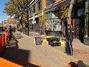 Calgary Bylaw officers oversee the seizure of property in front of Without Papers Pizza, including a sign that says 