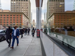 Masked pedestrians walk in downtown Calgary with office buildings reflected in a window on Tuesday, Nov. 30, 2021.