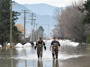 Rob Feenstra and Brendan van Biert walk through flood water after conducting a hazard assessment at a local bio gas plant in Abbottsford, B.C., on Nov. 22, 2021.