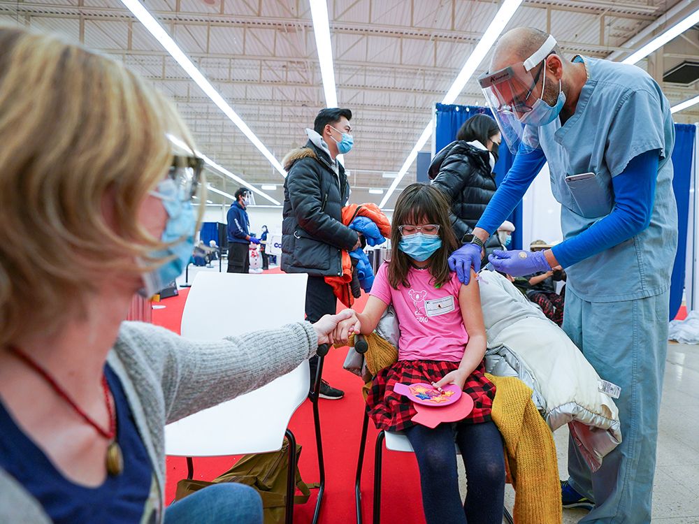  Kate Rhodes holds her mother’s hand as she gets her shot at a Humber River Hospital vaccination clinic in Toronto on Nov. 25, 2021.