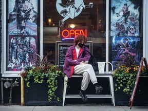 A person wearing a mask sits outside The Sidekick cafe and comic book shop in downtown Toronto on Oct. 14, 2021.
