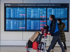 Travellers walk by a flight information screen at Calgary International Airport (YYC) where most of the flights have been delayed and some cancelled on Monday, December 27, 2021.
