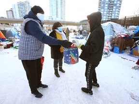 Moses and Jennifer Ndirangu (L) hand out small gifts of clothing and treats at the Drop-In Centre in downtown Calgary on Saturday, December 25, 2021. Their family has made a tradition of making sure vulnerable and homeless people have some warm clothing and food at Christmastime. Many of the clients choose to live in tents on the street in front of the Drop-In Centre, despite the ambient temperatures dipping to -25 C or colder at night.