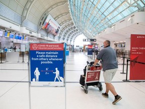 In this file photo, a man pushes a baggage cart while wearing a mandatory face mask at Toronto Pearson International Airport in Toronto, on June 23, 2020