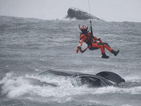 A U.S. Coast Guard diver is lowered from a hovering helicopter to pull a body from a submerged vehicle stuck in rushing rapids just yards from the brink of Niagara Falls, Dec. 8, 2021.