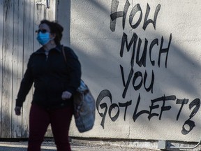 A pedestrian wearing a mask walks past graffiti stating "How Much You Got Left?" outside of a TD Canada Trust location in Toronto during the pandemic.