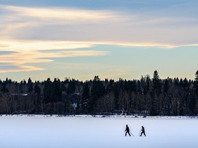 Two people go for a walk on the frozen Glenmore Reservoir as a chinook arch is visible in the sky on Monday, January 10, 2022.