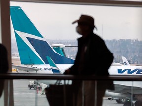 Travellers move between gates with a WestJet plane in the background at the Calgary International Airport on Tuesday, January 18, 2022. WestJet announced it would be consolidating or cancelling up to 20 per cent of its flights through Feb. 28.