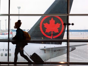 Reisende bewegen sich am Dienstag, den 18. Januar 2022, zwischen den Gates mit einem Flugzeug von Air Canada im Hintergrund auf dem Calgary International Airport.