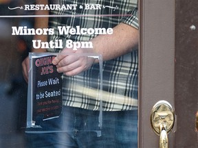 A person removes the vaccine proof sign from behind the door at Original Joe’s on Stephen Avenue on Wednesday, February 9, 2022 the day after Premier Jason Kenney announced the end of the Restriction Exemption Program in Alberta.