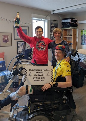 Stewart Midwinter posiert für ein Foto, nachdem er 40.075 km auf seinem FES-Rad zurückgelegt hat.  Er feierte mit Jorge Errasquin, seinem Physiotherapieassistenten, und Julie Muller, seiner Ehefrau, Trainerin und Motivatorin.