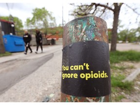 Pedestrians make their way past a sticker raising awareness about opioids in an alley near 81th Avenue and Calgary Trail, in Edmonton Friday May 28, 2021.