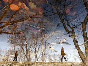 The reflection of pedestrians on a walk along the Bow River pathway in Eau Claire is seen in a puddle made by the melting snow on Monday, March 14, 2022.